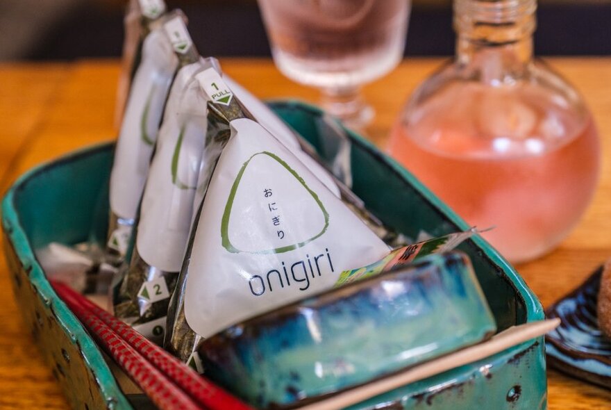 Three onigiri wrapped in plastic on a blue ceramic tray.