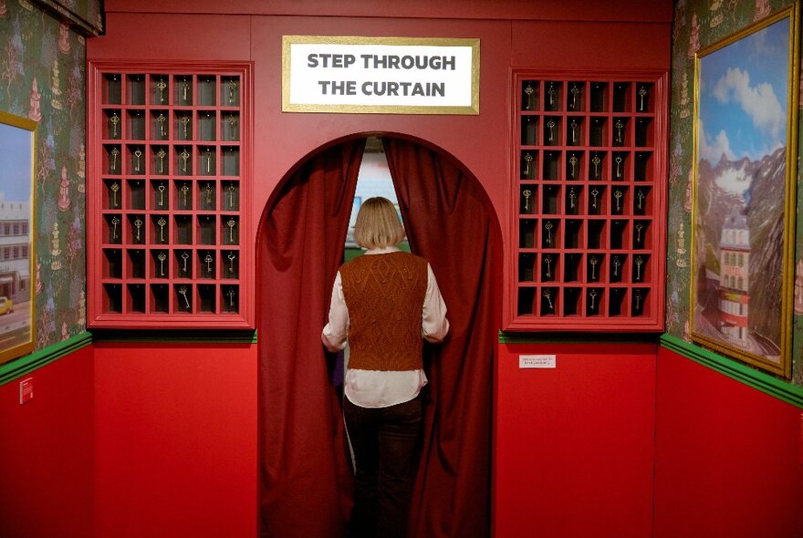 A person entering a curtained room through a red archway.