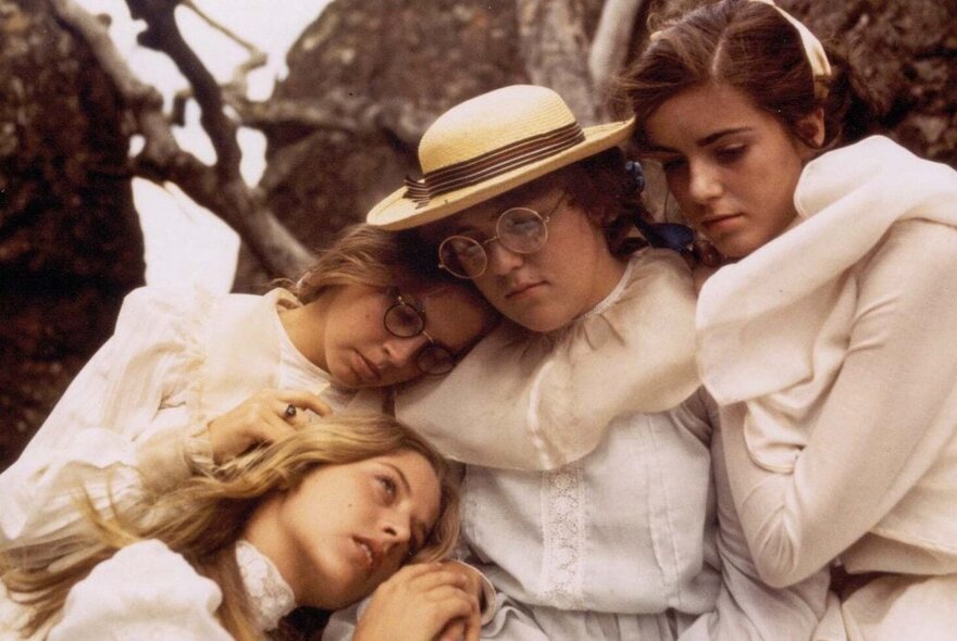 A still from the movie, Picnic at Hanging Rock, where four young girls in white turn-of-the-century clothing are hugging each other in despair.