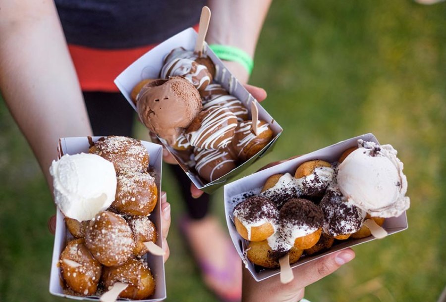 Two people holding Greek doughnuts in takeaway boxes.