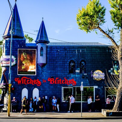 The exterior of the venue Witches in Britches, with people on the street outside, and a tree on the right.