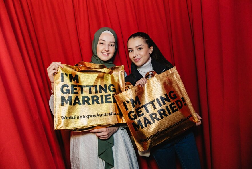 Two people smiling while holding an I'm Getting Married bag. 