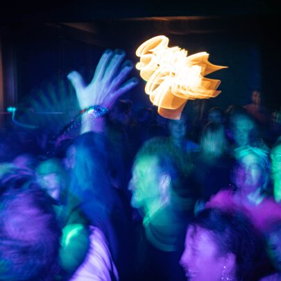 A blurred picture of people on a dancefloor with green and purple lights and a blurred flare of yellow in the middle. 