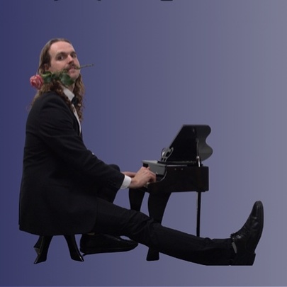 A person wearing a black suit and shoes seated at a miniature grand piano while extending one leg straight out in front, against a blue background.