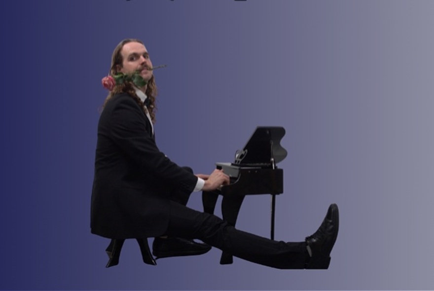 A person wearing a black suit and shoes seated at a miniature grand piano while extending one leg straight out in front, against a blue background.