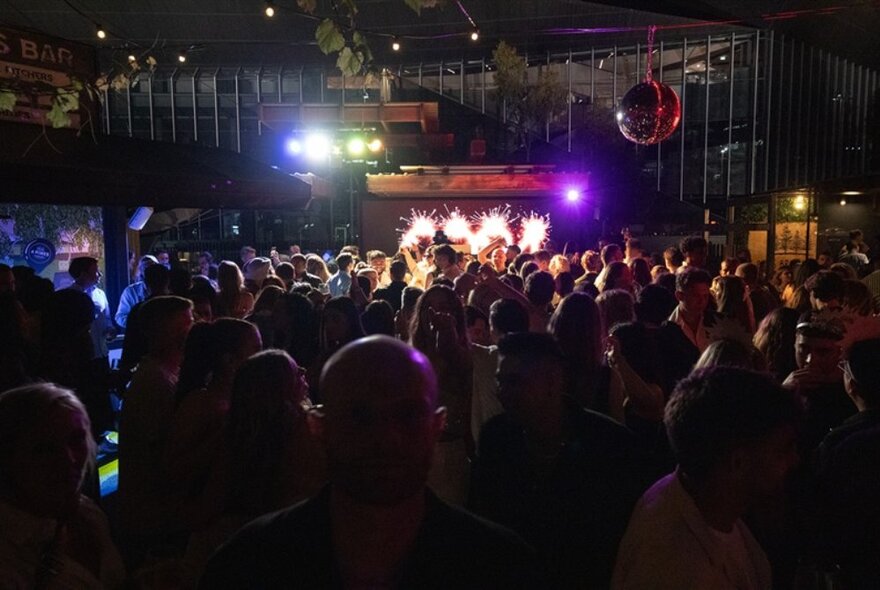 People in a nightclub venue, a stage and lights at the far end of the room. 