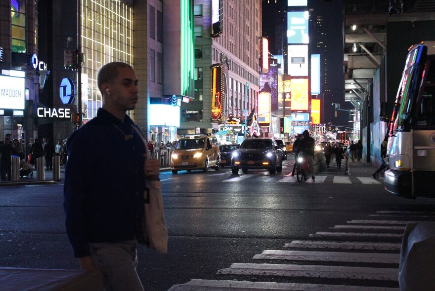 A darkened image of a man crossing a busy New York street at night.