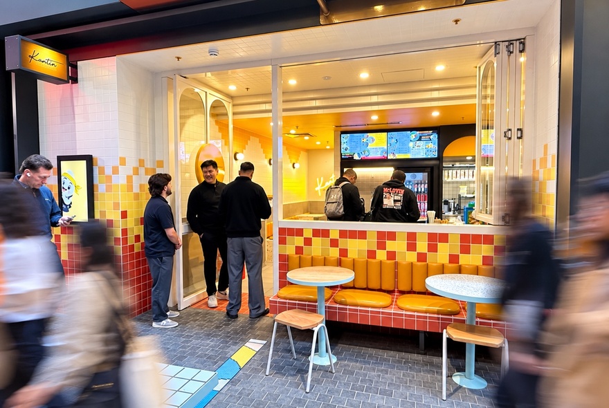 The bright yellow storefront and outdoor seating area of Kantin Indonesian restaurant at Melbourne Central, with people inside ordering food and queued near the door.