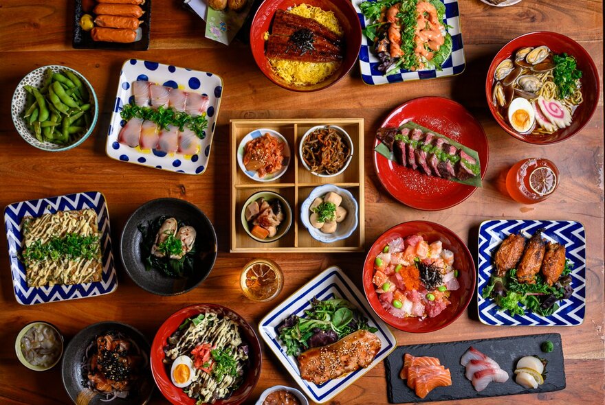 Looking down at a table filled with plates and trays of Japanese food.