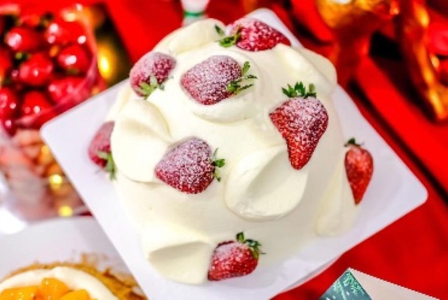 Strawberry cream cake on a white plate against a background of desserts on red.