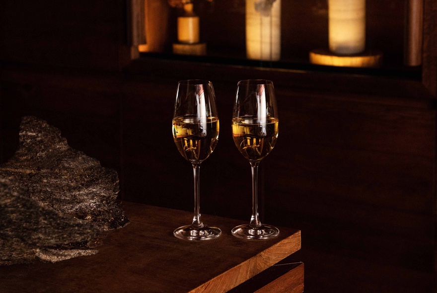 Dark table setting with two glasses of white wine.