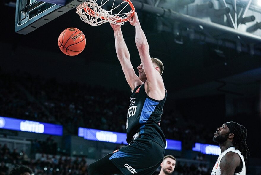 A basketball player hanging from the hoop after dunking a basketball through it, on a basketball court.