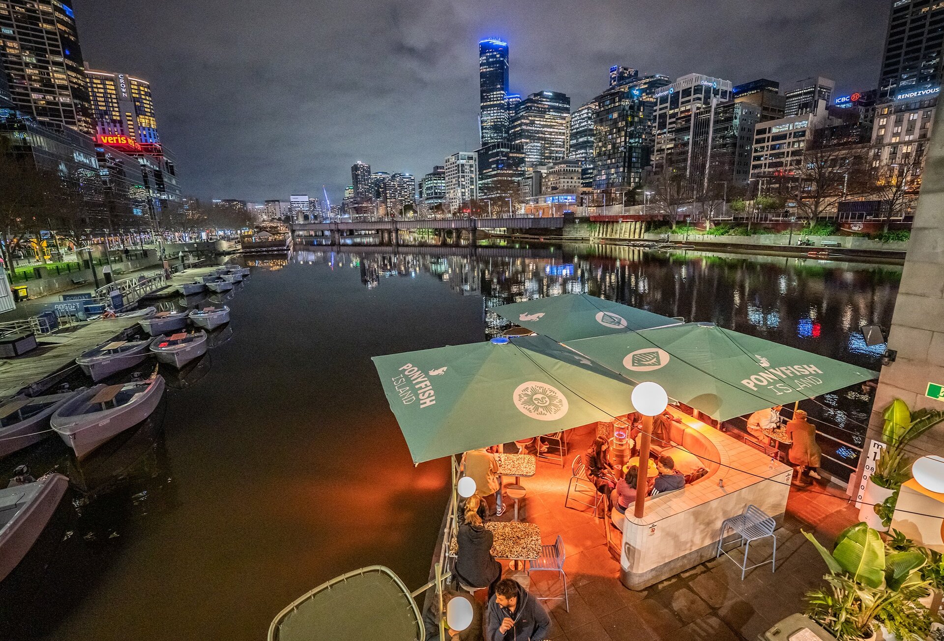A bar on a river at night with Melbourne's city skyline in the background.