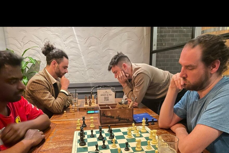 Two groups of people playing chess at a table, concentrating on the game.