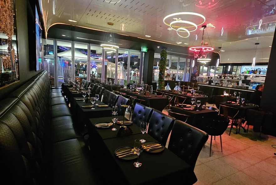 Interior of a large dining area with a long black banquette and neon spiral lights.l