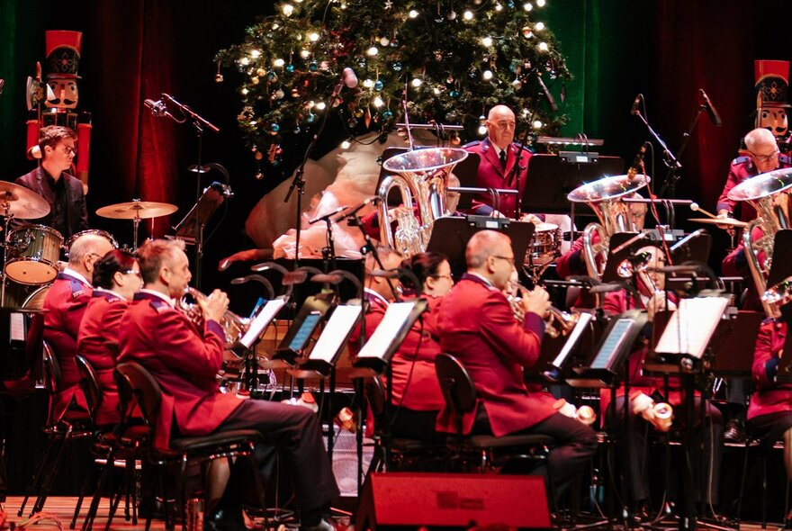 An orchestra dressed in red suits playing on a stage that is decorated in festive and seasonal Christmas decorations.