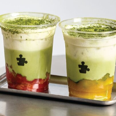 Strawberry and mango flavoured matcha drinks in plastic cups on a silver tray