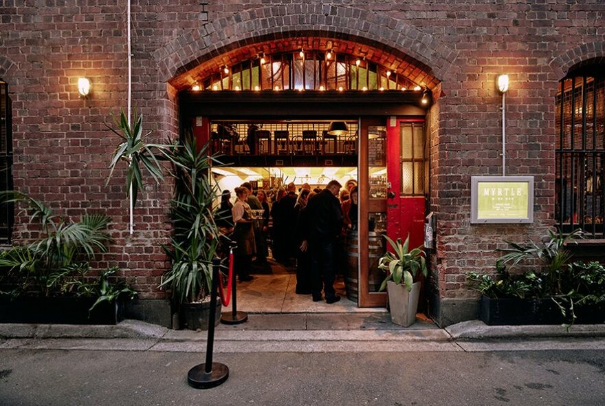 Exterior of Myrtle Wine Bar in a laneway with plants, lighting and ornate doorway.