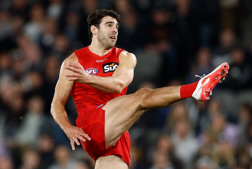 A Gold Coast Suns AFL player with his leg in the air after kicking a football during a game.