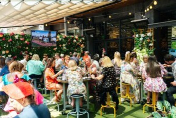 Women in colourful dresses sitting at an outdoor bar in the sun. 