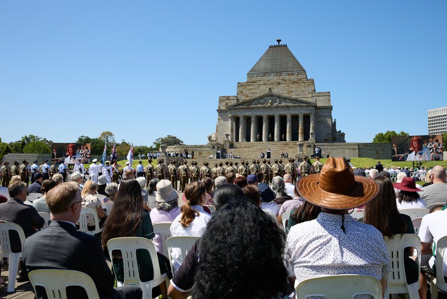 The back of a seated crowd assembled outside the Shrine of Remembrance. 