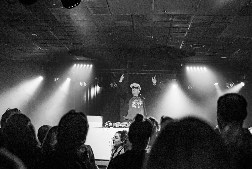 Black and white image of a DJ performing in front of a small group of people. 