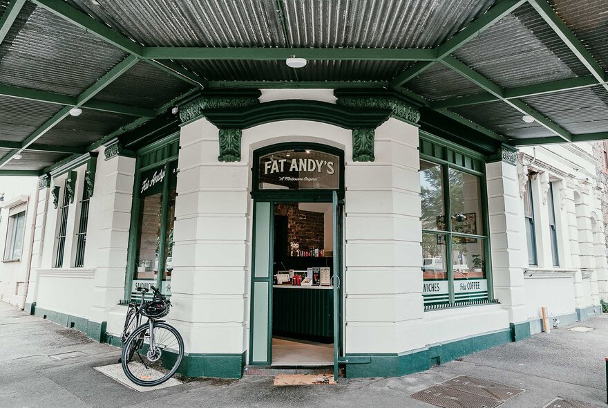 The corner site of Melbourne sandwich shop, Fat Andy's, with cream brickwork and dark green accents and a bicycle parked out the front.