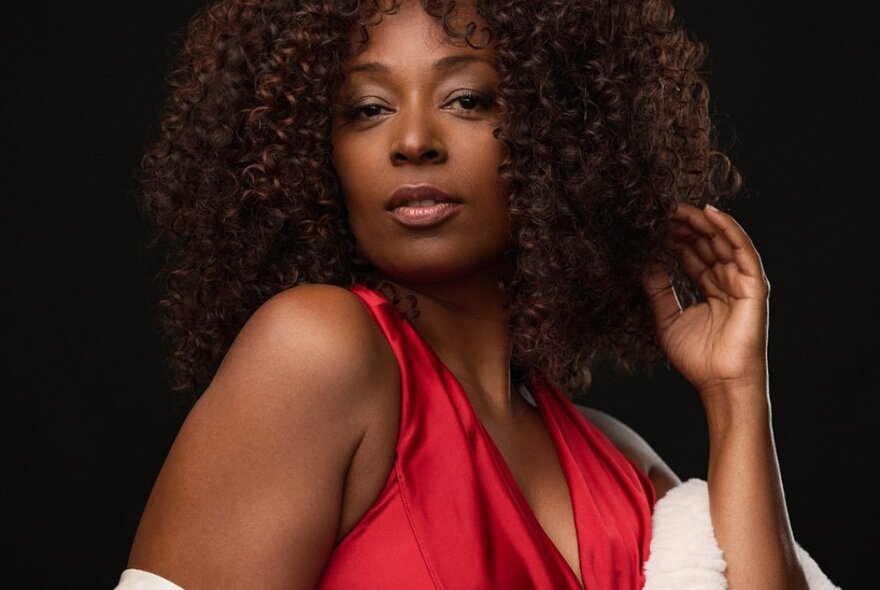 Singer Linzy Bacbotte, her thick curly hair framing her face, wearing a red V-neck dress and posed in front of a dark background.