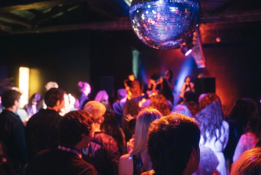 People dancing in a small room under a large mirrorball. 