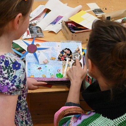 A child and their adult carer, engaged in a collaborative collage arts and crafts activity, involving paper and other materials.