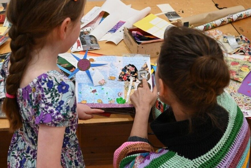 A child and their adult carer, engaged in a collaborative collage arts and crafts activity, involving paper and other materials.