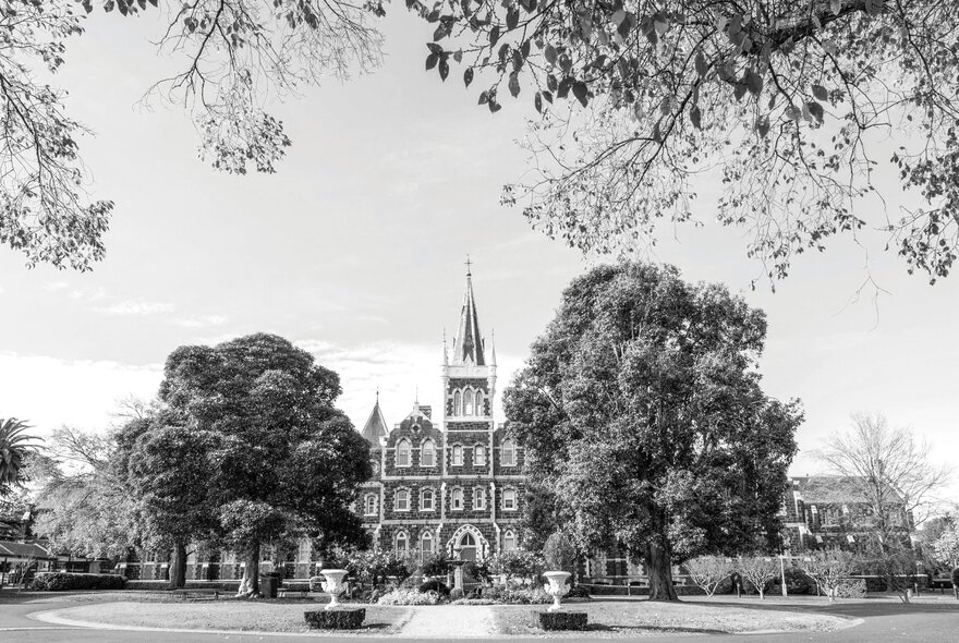 A black and white picture of Deaf Children Australia's historic Bluestone building with a pointy tower in a large garden setting. 