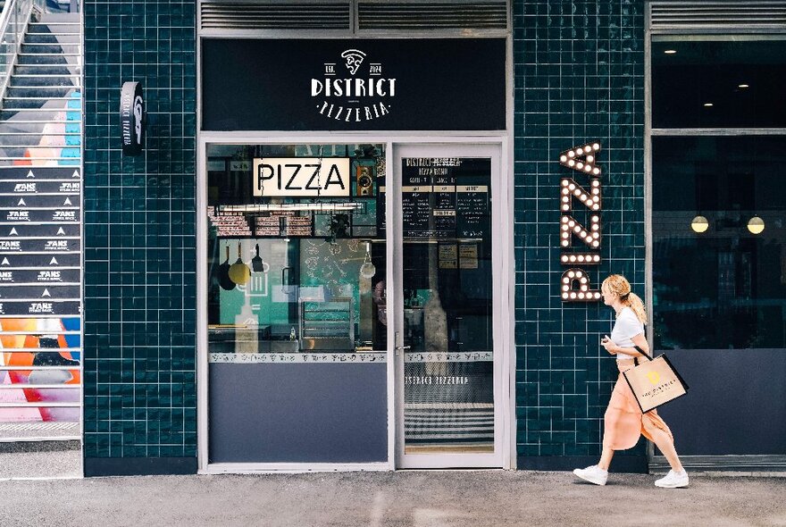 A woman walking past the door of a pizza restaurant