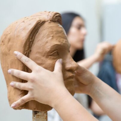 Hands working on a sculpture of a head using clay. 