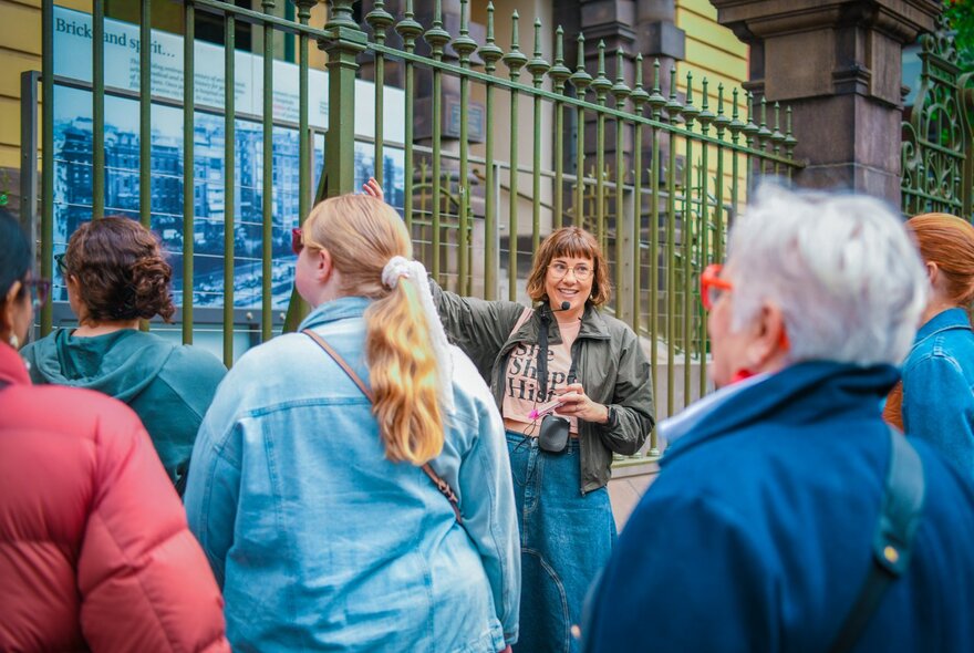 A woman leading a walking tour, standing in front of an iron fence as she talks to the group.