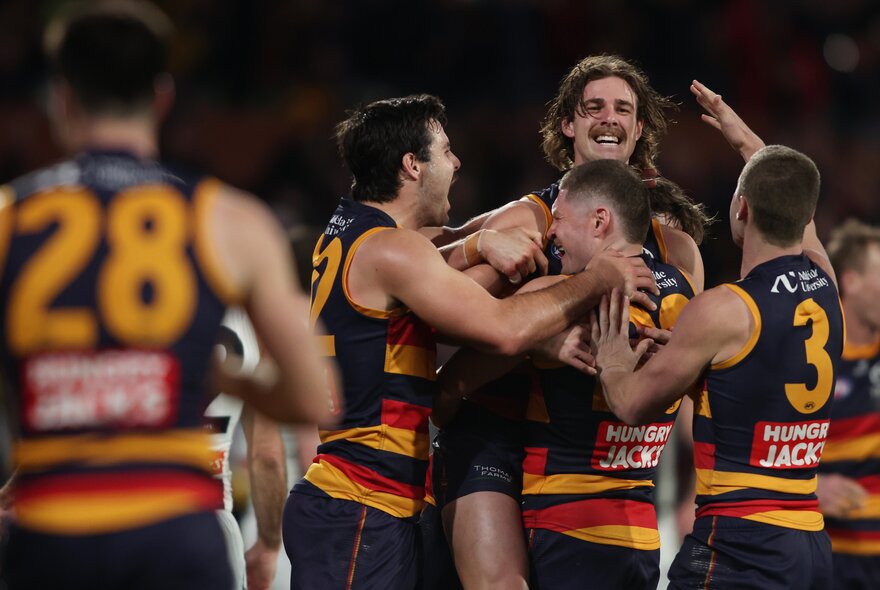 A huddle of Adelaide Crows AFL players hugging and congratulating each other on the football field.