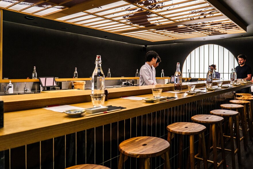 A sushi bar with stools around it and a sushi chef making sushi. 