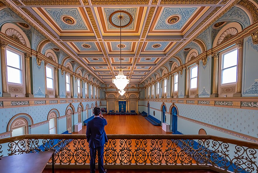 A man standing on the balcony in an ornate blue room.