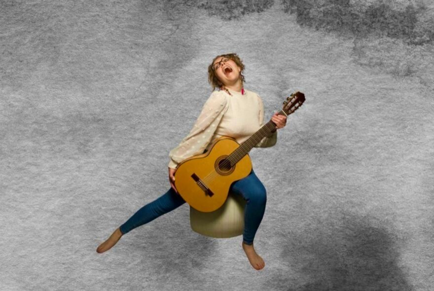 Woman holding an acoustic guitar, seated on a ball amid clouds, her head back singing.