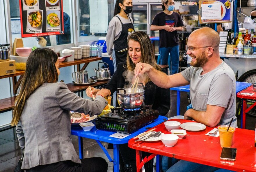 Three diners reaching with chopsticks around a hotpot.