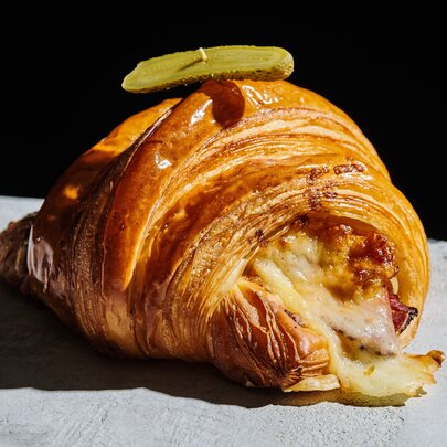 A Reuben croissant placed on a concrete bench.