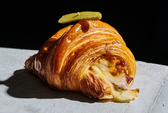 A Reuben croissant placed on a concrete bench.