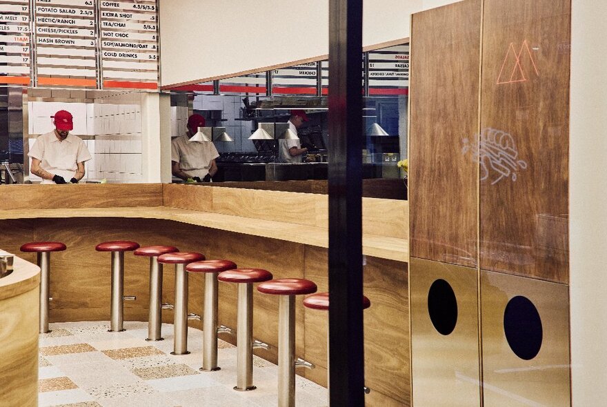 The interior of Hector's Deli showing red bar stools around a curved wooden counter, a large menu on the wall above the kitchen where a person is preparing food.