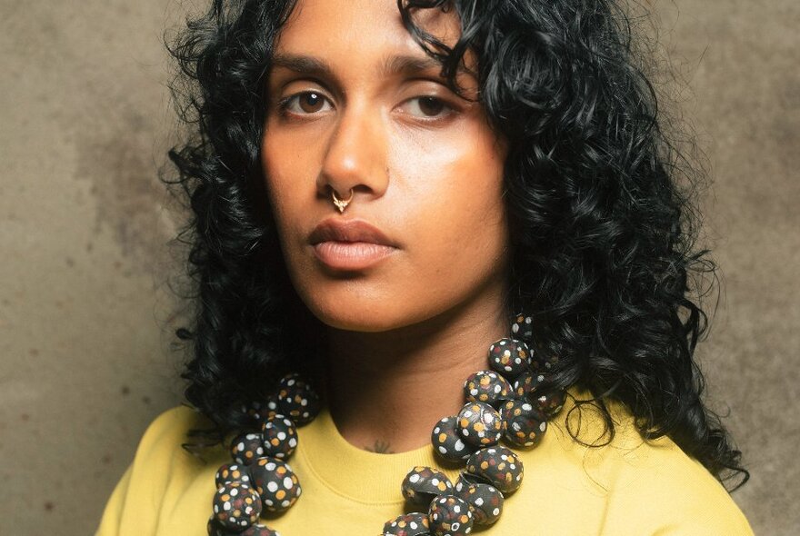 A curly-haired woman looking very serious with an oversized spotty necklace. 