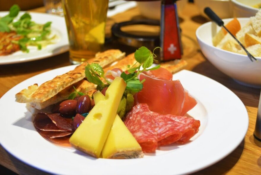 Cheese and meat platter with slices of Swiss cheese, foccacia and olives.