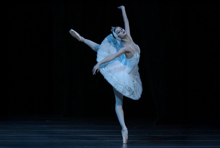 Ballerina wearing a white tutu with arms and legs stretched.