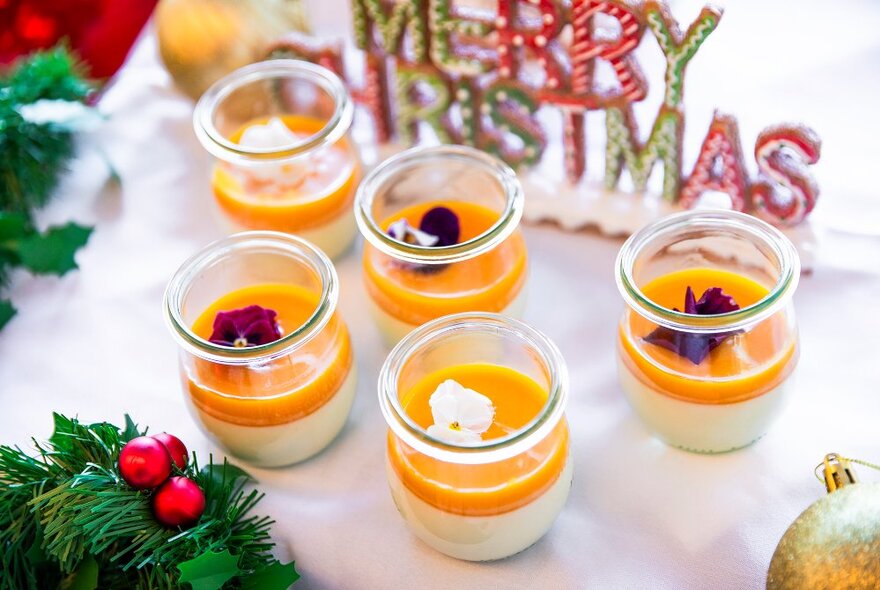 Pannacotta desserts with a mango puree and nasturtium flower garnish, in front of a 'merry christmas' sign.