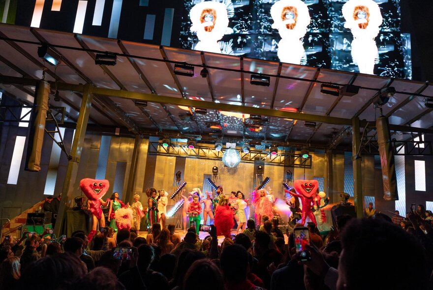 The main stage at Fed Square at night, filled with performers in colourful costumes, in front of an audience.