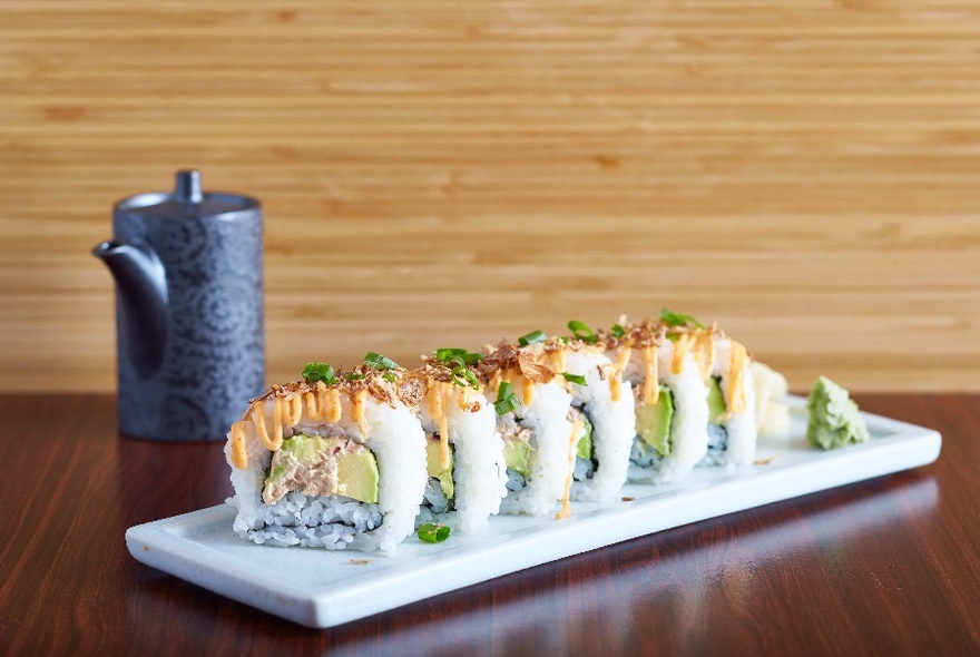 A plate of sliced avocado sushi rolls and a pot of tea.