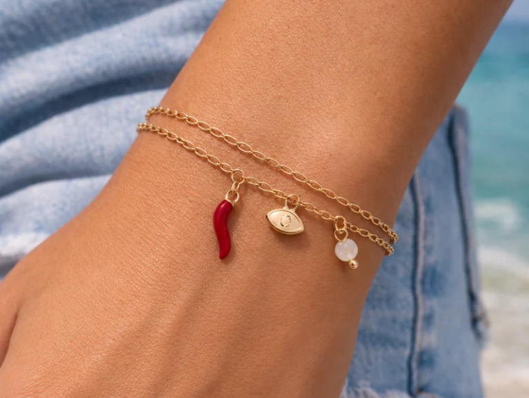 A model wearing two bracelet chains with a cornicello, evil eye and pearl charm. 